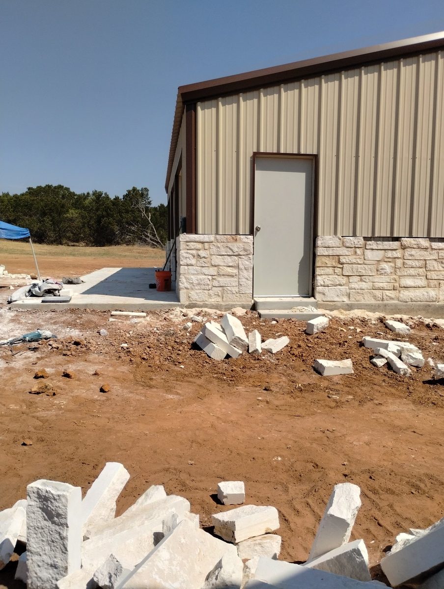 Stone masonry in Hamilton County, Texas — limestone wainscot being installed on a metal building by WhiteStone Construction